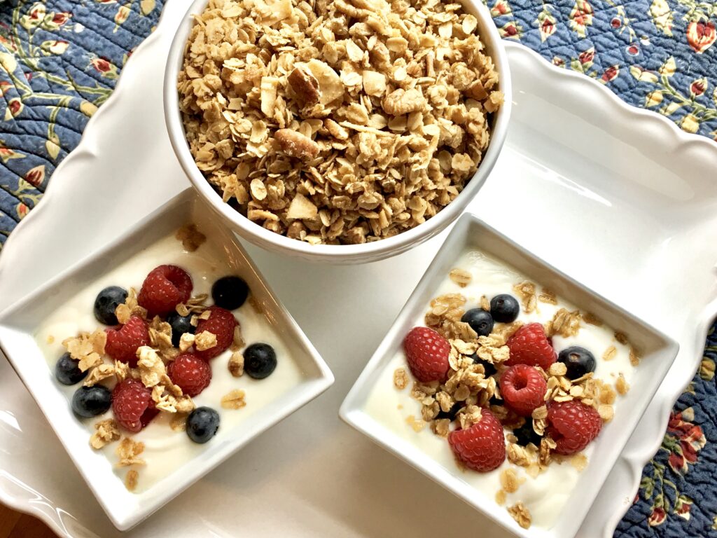 serving bowl of granola and two small square servings of the granola over yogurt with berries