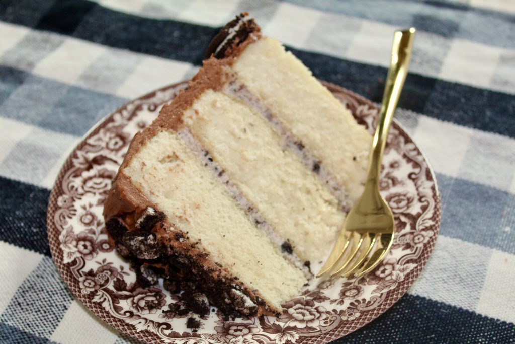 Slice of cake with oreo vanilla buttercream inside and chocolate buttercream outside on a plate.