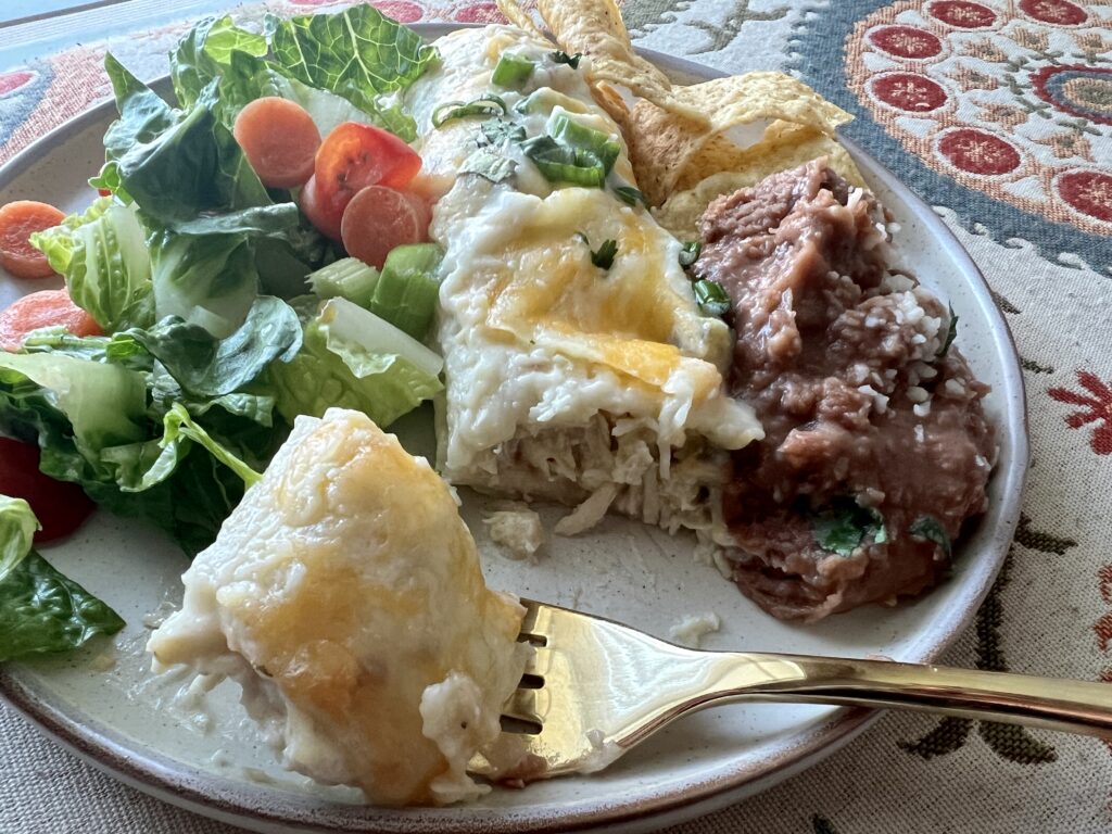 Dinner plate with creamy chicken enchiladas, salad and refrained beans