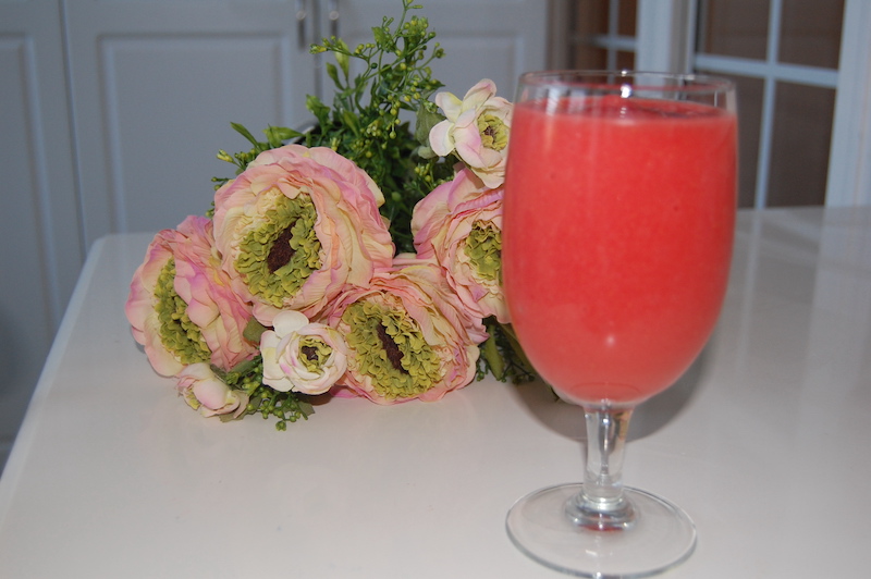 Frozen Strawberry lemonade in glass next to pink flowers.