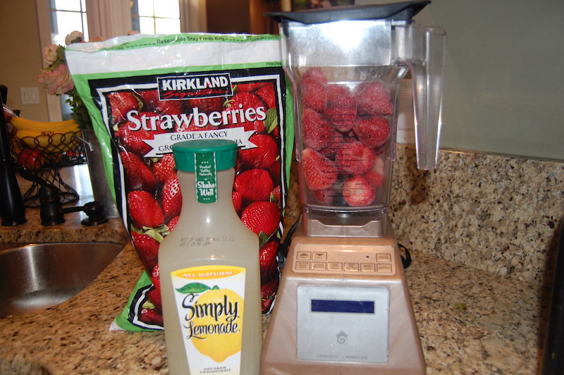 a blender full of frozen strawberries and a jug of lemonade