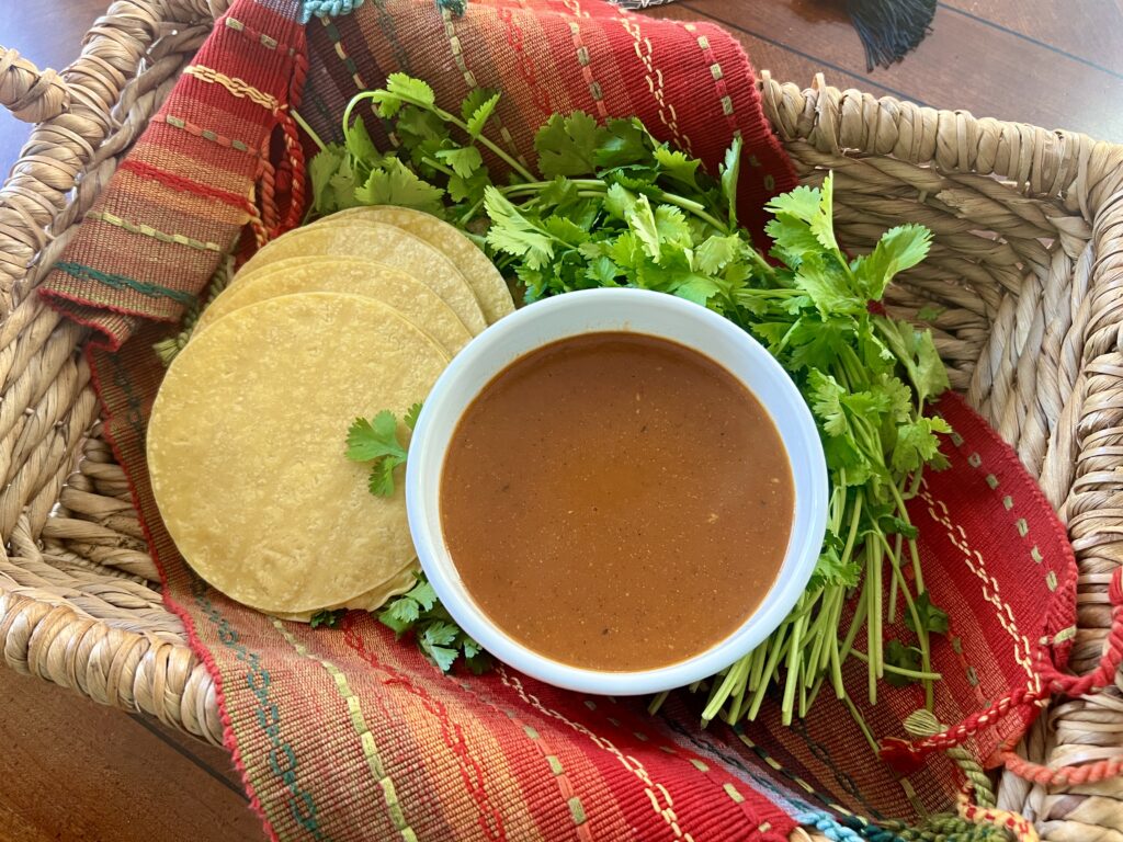 bowl of red enchilada sauce in a basket with corn tortillas and cilantro